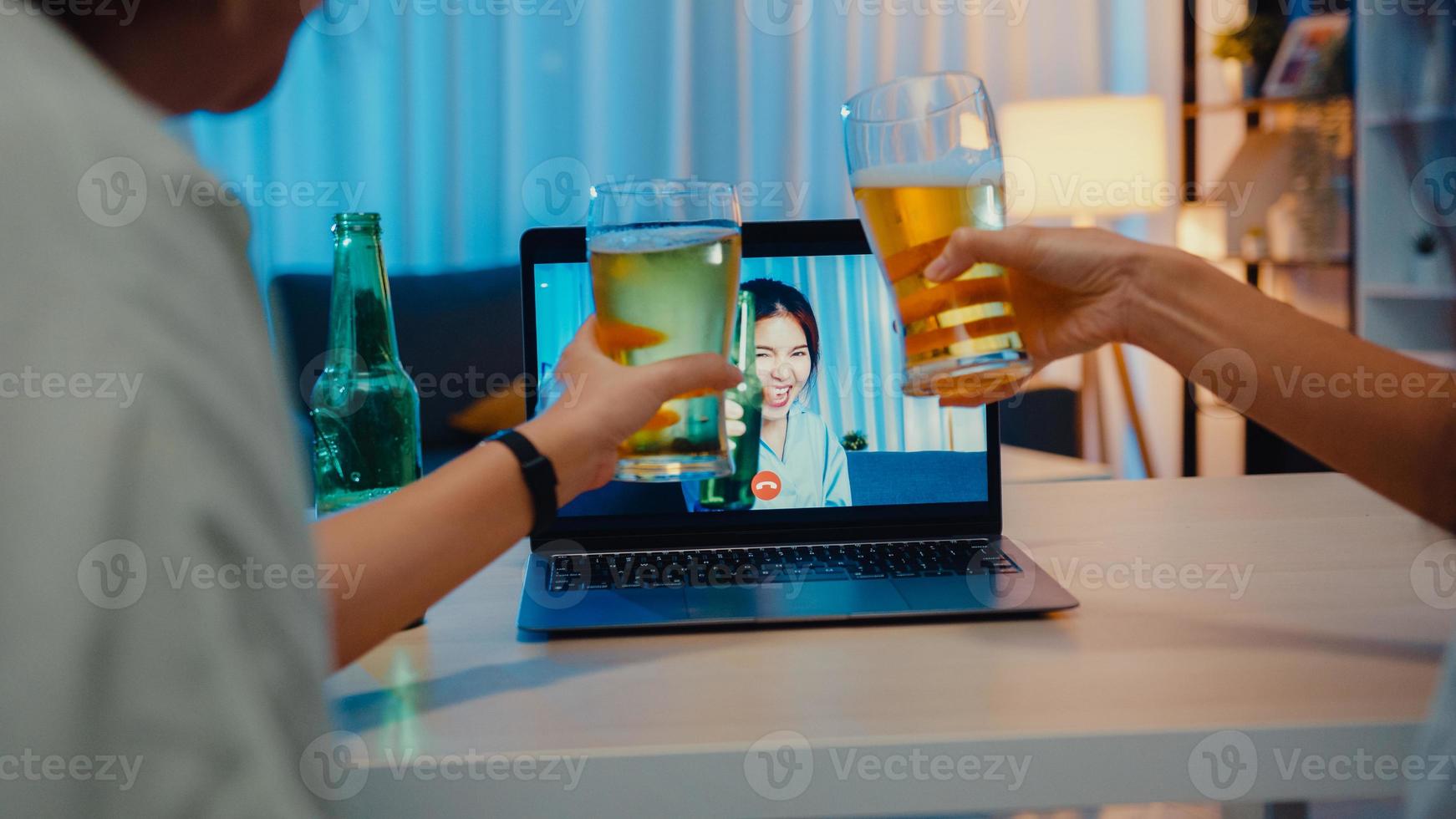 Joven mujer asiática bebiendo cerveza divirtiéndose feliz momento fiesta nocturna evento celebración en línea a través de videollamada en la sala de estar de la casa por la noche. distanciamiento social, cuarentena para la prevención del coronavirus. foto