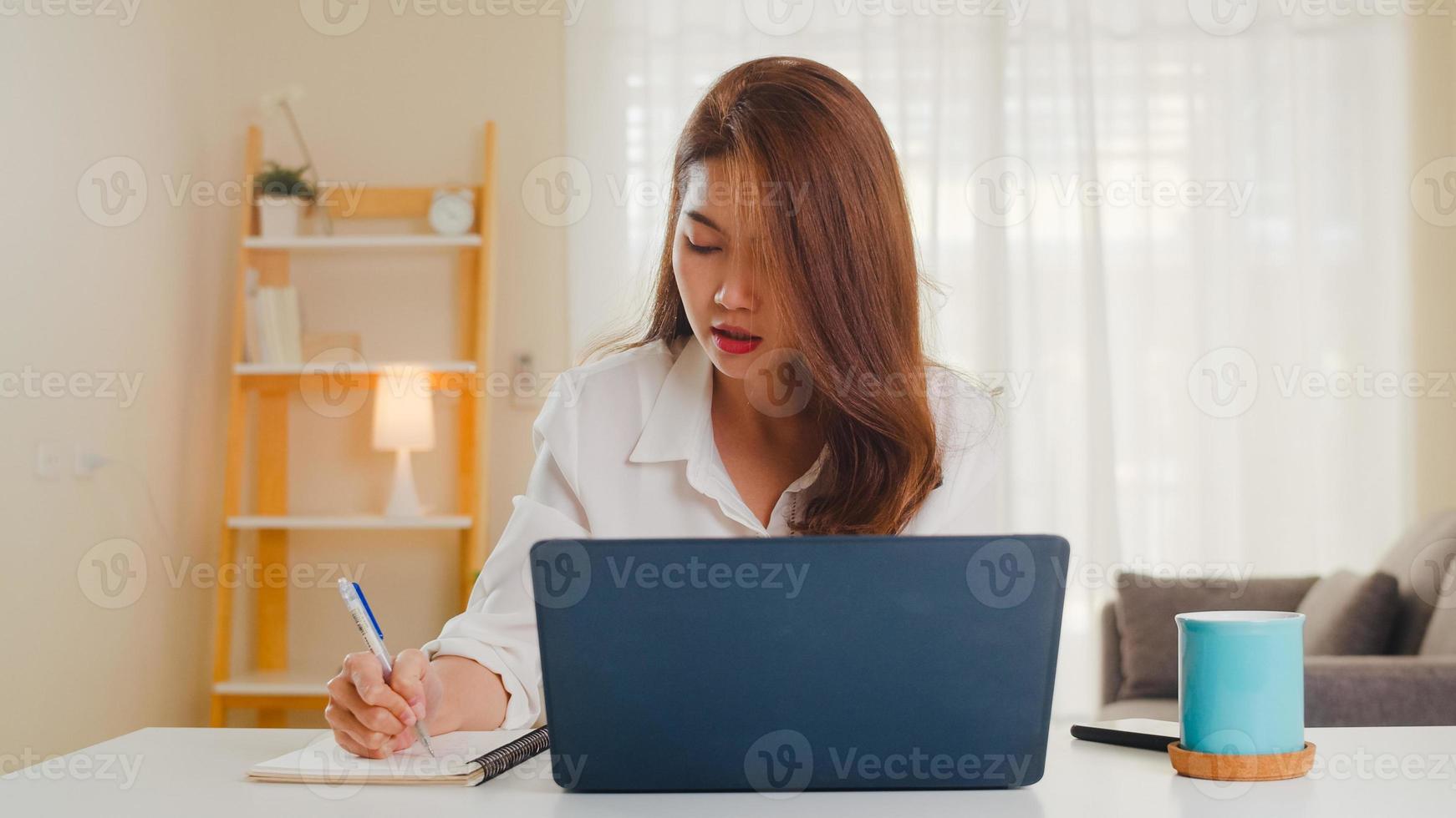 Retrato de ropa casual de mujeres asiáticas independientes usando una computadora portátil que trabaja en la sala de estar en casa. trabajo desde casa, trabajo a distancia, autoaislamiento, distanciamiento social, cuarentena para la prevención del coronavirus. foto