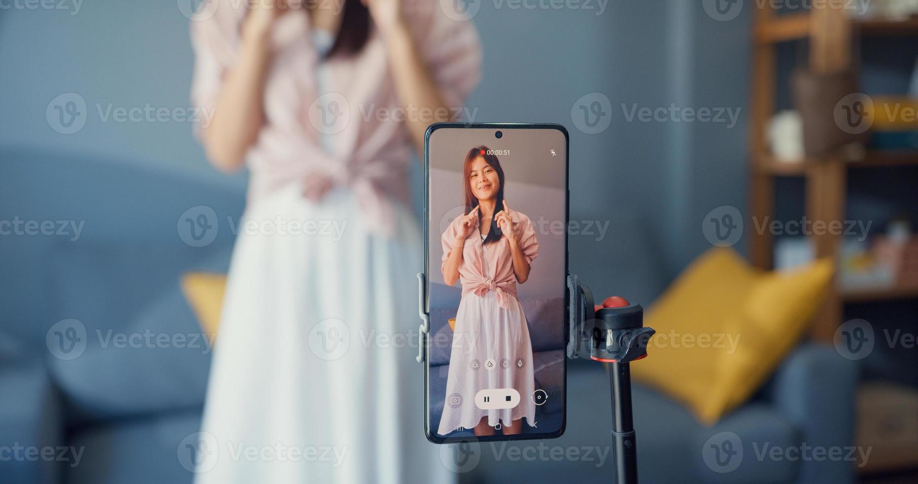 Happy young Asian girl blogger front of phone camera record video enjoy with dance content in living room at home. Social distance coronavirus pandemic concept. Freedom and active lifestyle concept photo