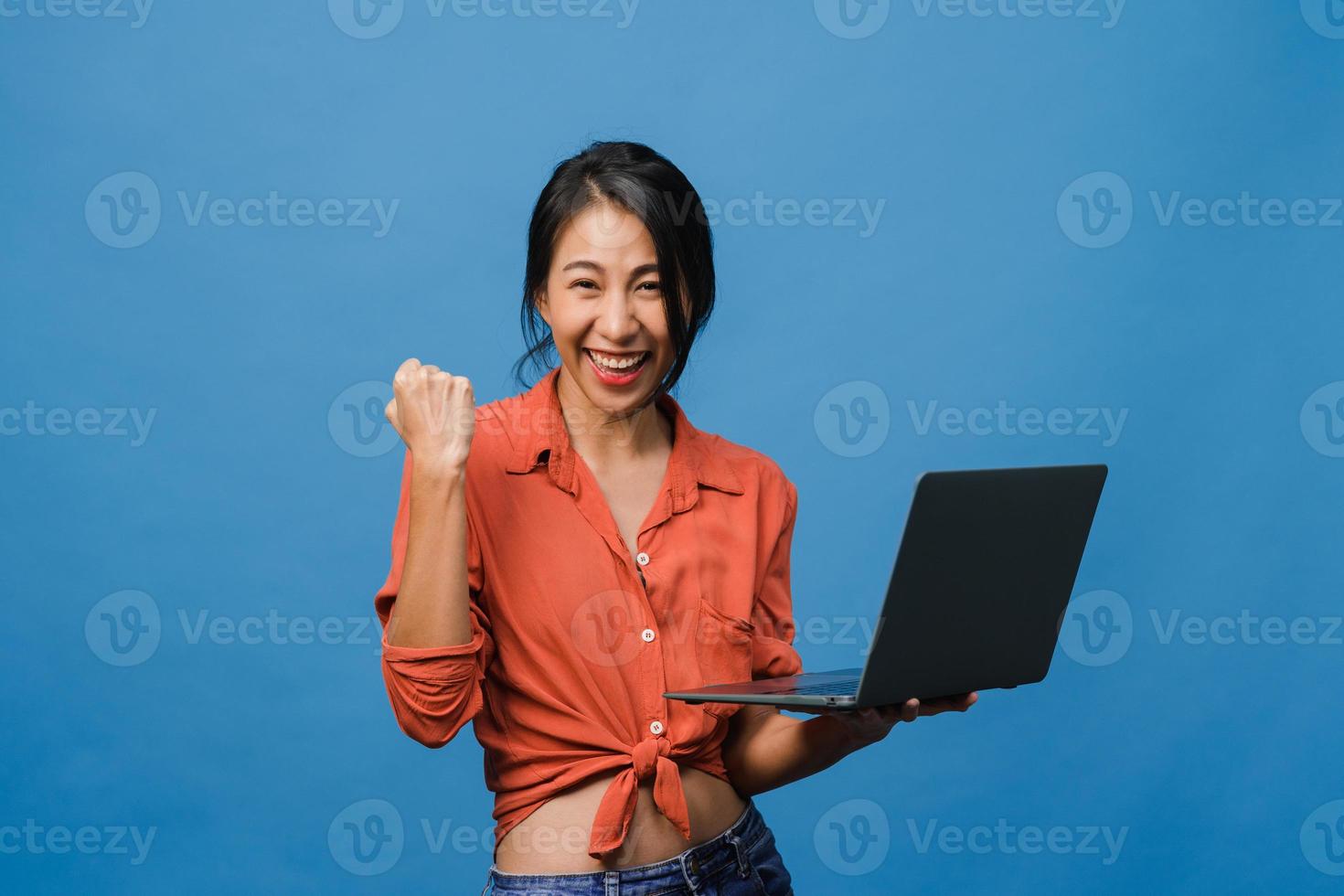 Young Asia lady using laptop with positive expression, smiles broadly, dressed in casual clothing feeling happiness and stand isolated on blue background. Happy adorable glad woman rejoices success. photo