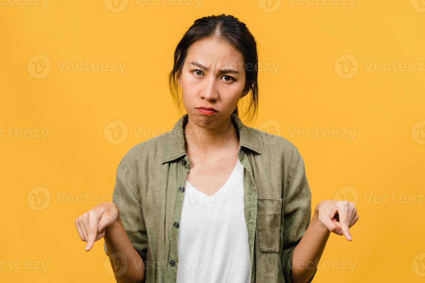 Young Asia Lady shows something amazing at blank space with negative expression, excited screaming, crying emotional angry looking at camera isolated over yellow background. Facial expression concept. photo