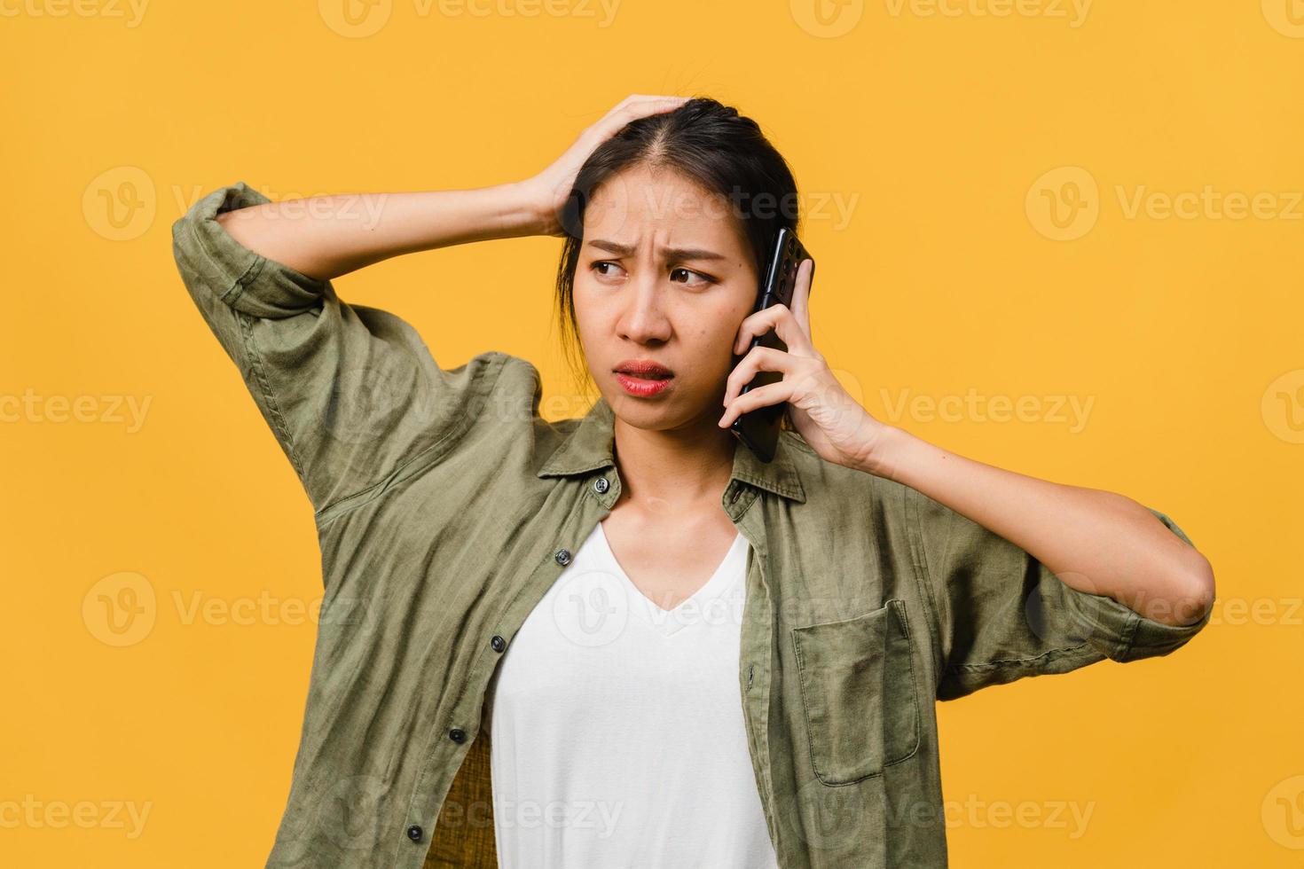 Young Asia lady talk by phone with negative expression, excited screaming, cry emotional angry in casual cloth and stand isolated on yellow background with blank copy space. Facial expression concept. photo