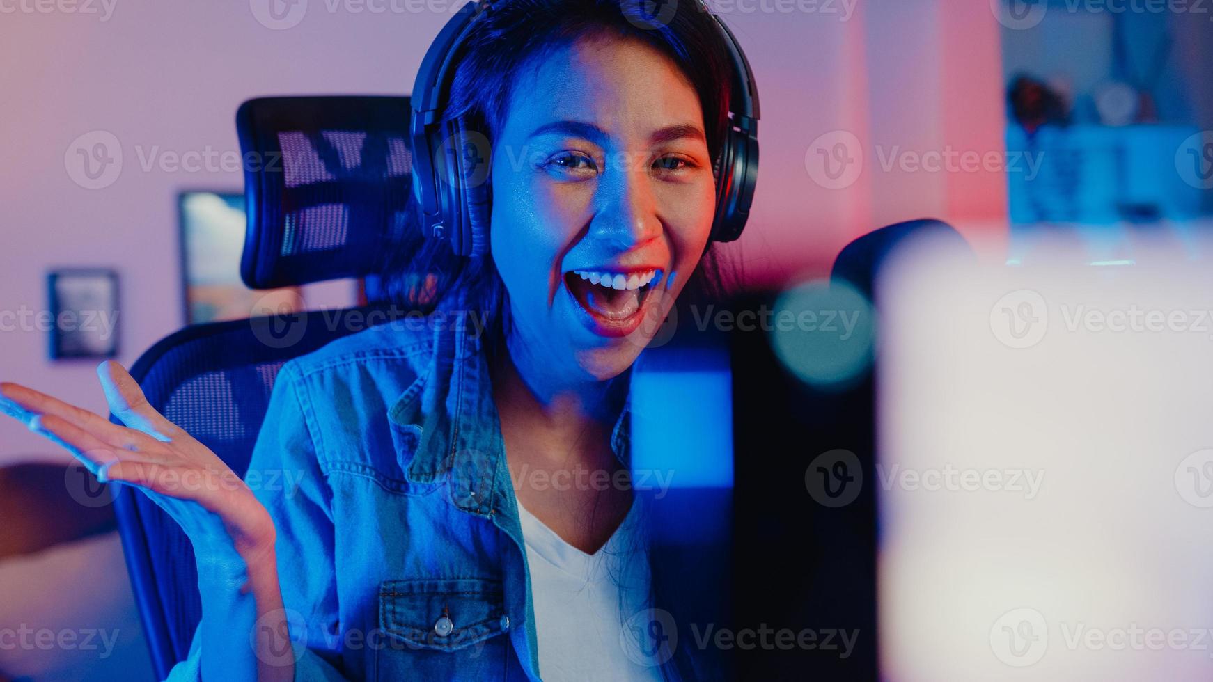 Happy asia girl blogger music influencer use smartphone broadcast recording wear headphone online live talk with listening audience in living room home studio at night. Content creator concept. photo