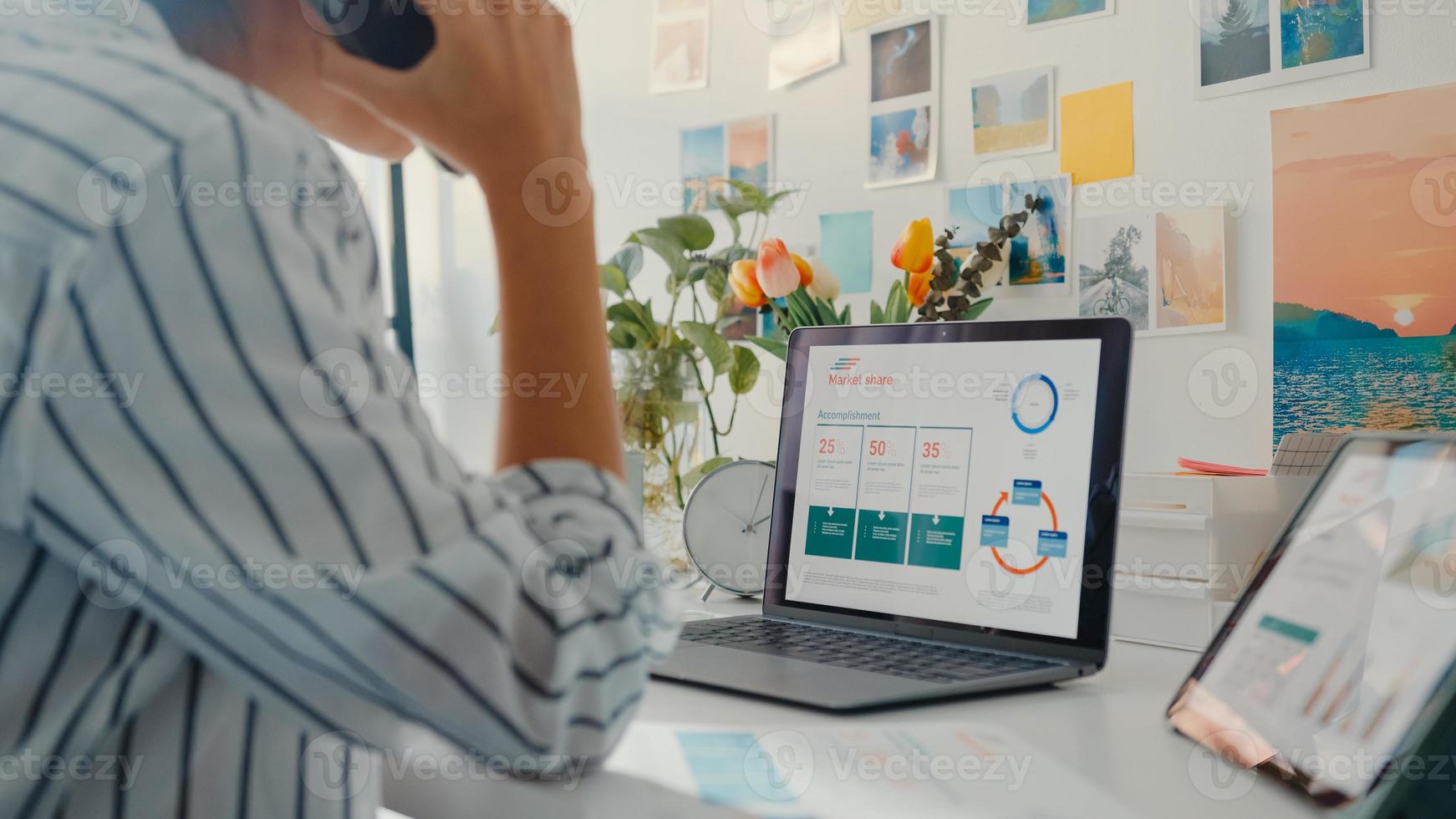 Young asia business lady call mobile phone with colleagues at company about work finance graph chart market plan in laptop and tablet at house. Girl student learn online, Work from home concept. photo