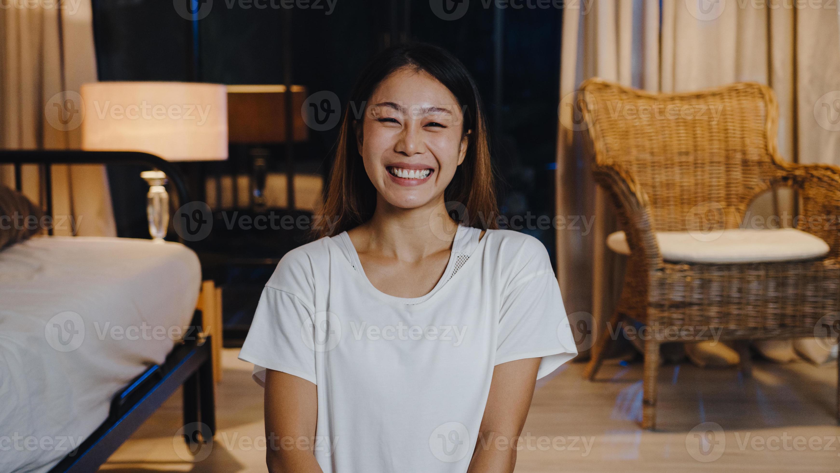 Cheerful young Asia lady feeling happy smile and look at camera using phone  make live video call in living room at home night. Social distancing,  quarantine for coronavirus. Close up webcam view.