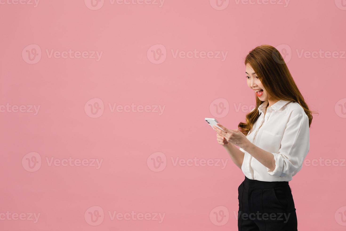 Señora joven de Asia que usa el teléfono con expresión positiva, sonríe ampliamente, vestida con ropa casual sintiendo felicidad y de pie aislado sobre fondo rosa. feliz adorable mujer alegre se regocija con el éxito. foto