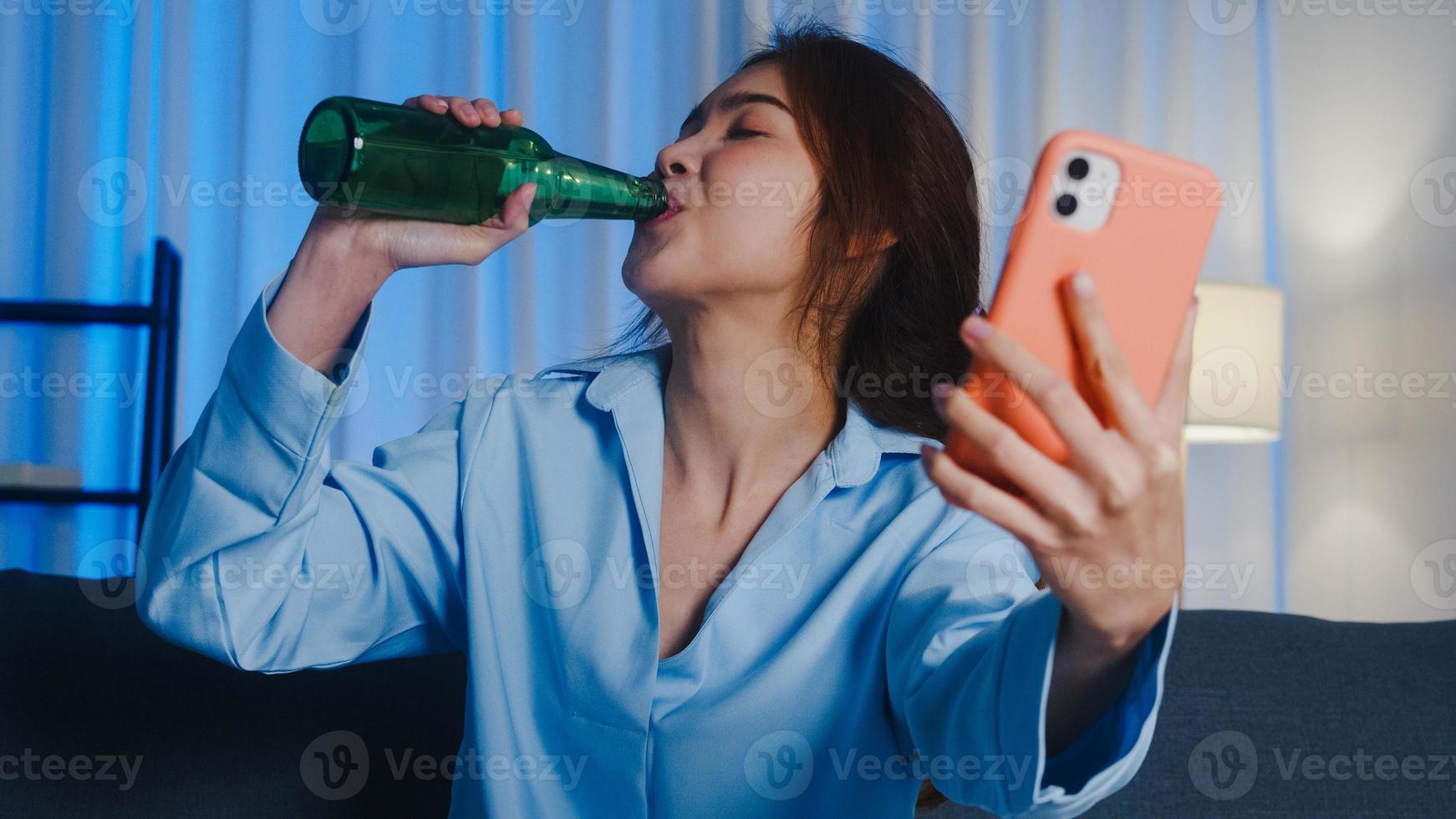 joven asiática bebiendo cerveza divirtiéndose feliz momento fiesta nocturna evento celebración en línea a través de videollamada en la sala de estar en casa por la noche. distanciamiento social, cuarentena para la prevención del coronavirus. foto