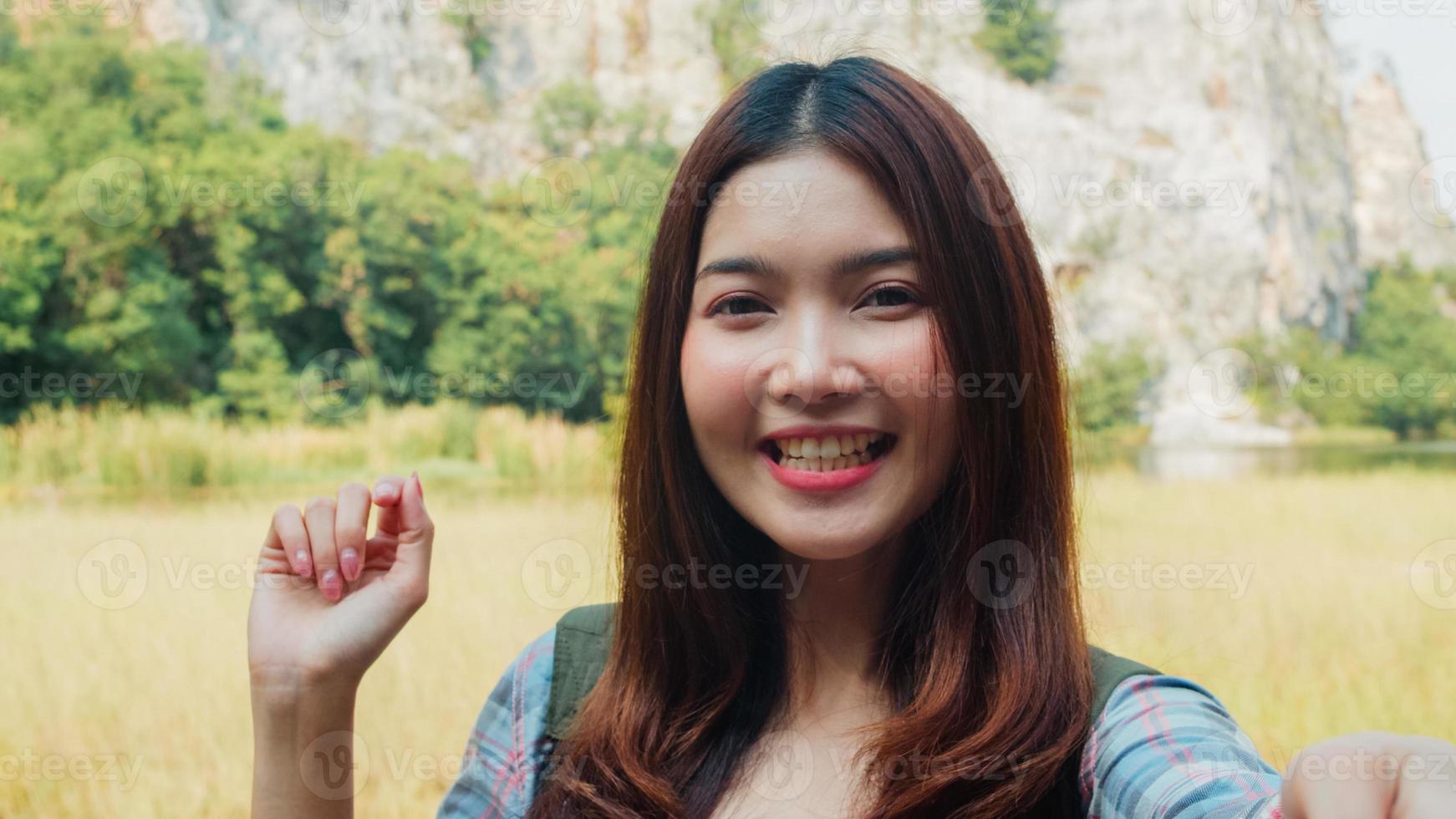 Cheerful young traveler Asian lady with backpack recording video vlog live streaming on phone upload in social media at mountain lake. Korean girl happy enjoy holiday trip. Lifestyle travel and relax. photo