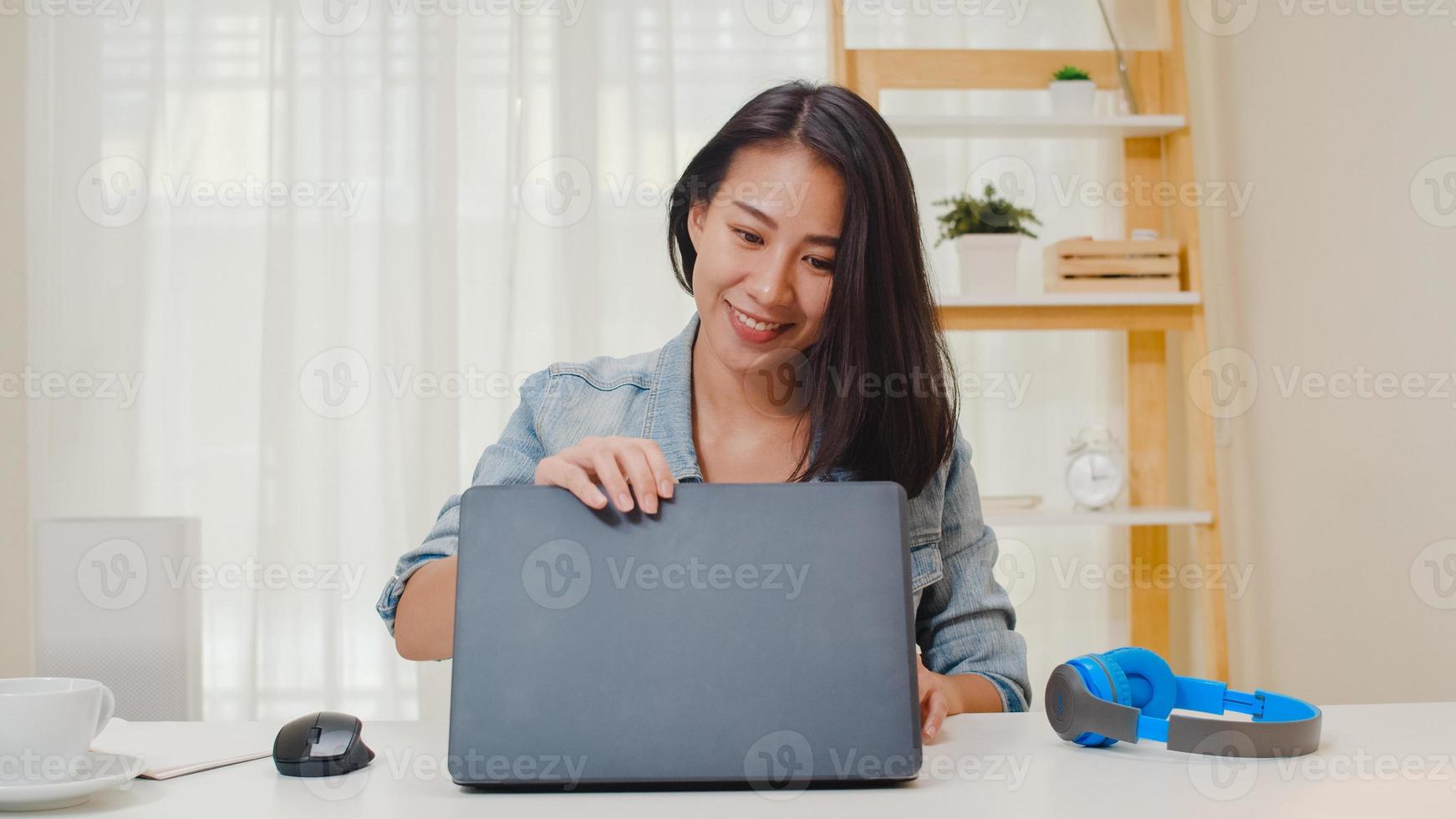 Retrato de ropa casual de mujeres de negocios inteligentes independientes usando laptop trabajando en el lugar de trabajo en la sala de estar en casa. feliz joven asiática relajarse sentado en la búsqueda de escritorio y hacer trabajo en internet. foto