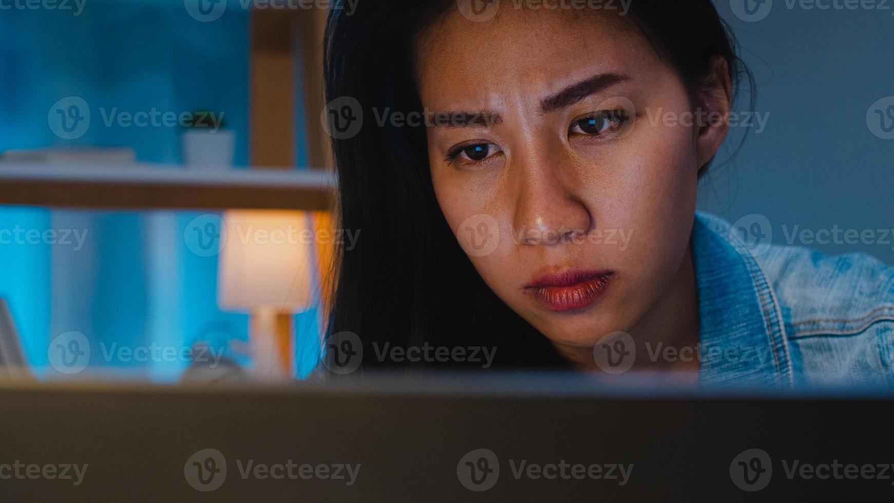 Millennial young Chinese businesswoman working late night stress out with project research problem on laptop in living room at modern home. Asia people occupational burnout syndrome concept. photo