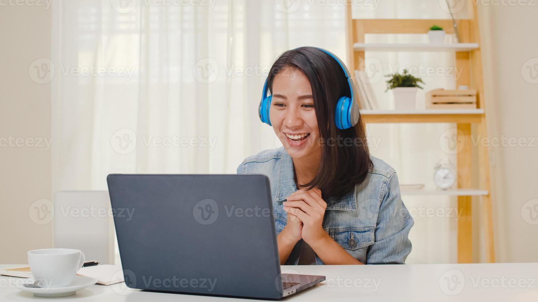 Mujeres de negocios independientes ropa casual usando una computadora portátil, llamada de trabajo, videoconferencia con el cliente en el lugar de trabajo en la sala de estar en casa. feliz joven asiática relajarse sentado en el escritorio hacer trabajo en internet. foto