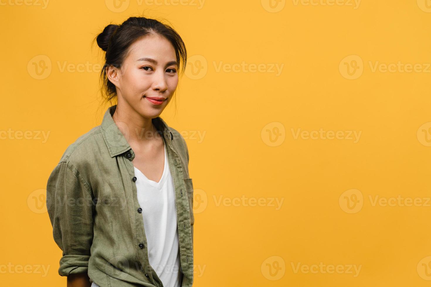 Jovencita asiática con expresión positiva, sonrisa amplia, vestida con ropa casual y mirando a cámara sobre fondo amarillo. feliz adorable mujer alegre se regocija con el éxito. concepto de expresión facial. foto