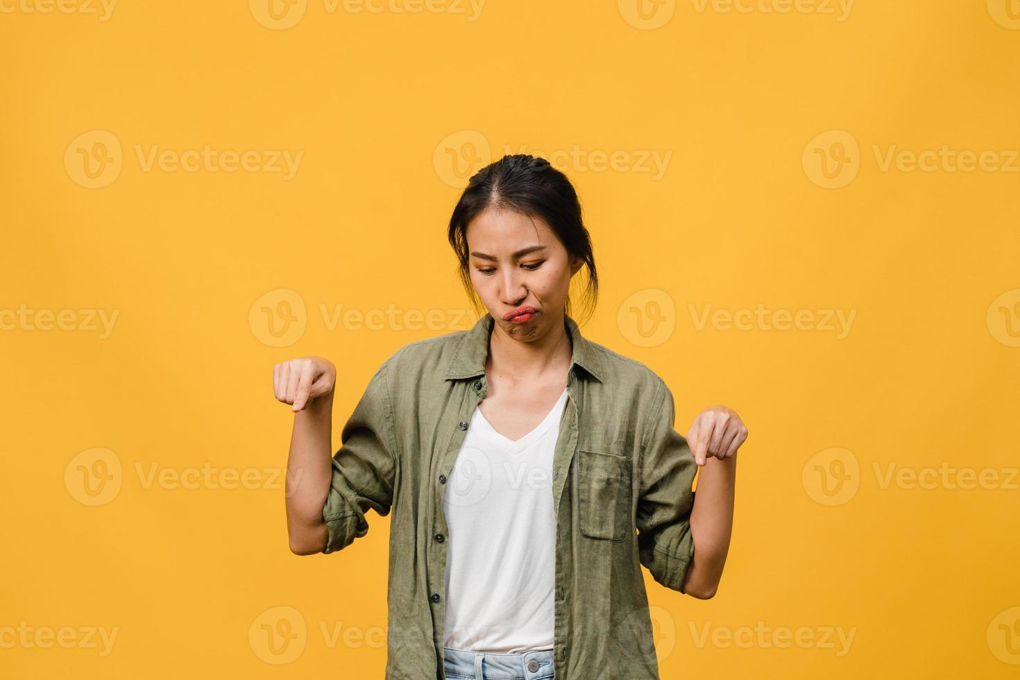 Joven mujer asiática muestra algo sorprendente en el espacio en blanco con expresión negativa, gritos emocionados, llorando enojado emocional en ropa casual aislada sobre fondo amarillo. concepto de expresión facial. foto