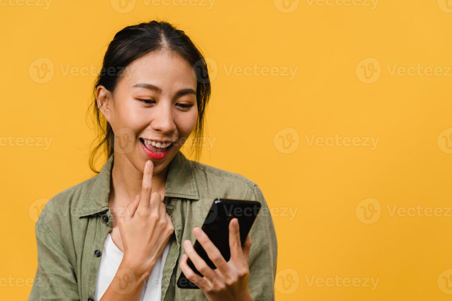 Young Asia lady using phone with positive expression, smiles broadly, dressed in casual clothing feeling happiness and stand isolated on yellow background. Happy adorable glad woman rejoices success. photo