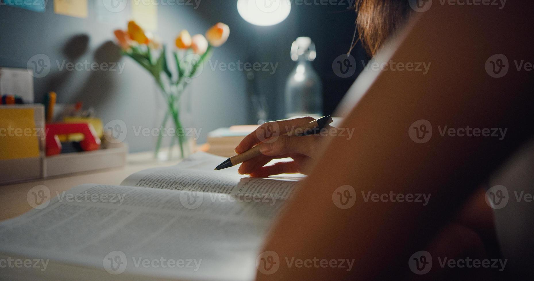 Young Asia teen girl student distance learning lesson and doing homework sitting at desk in living room at house night. Work from home, Social distancing, quarantine for corona virus prevention. photo