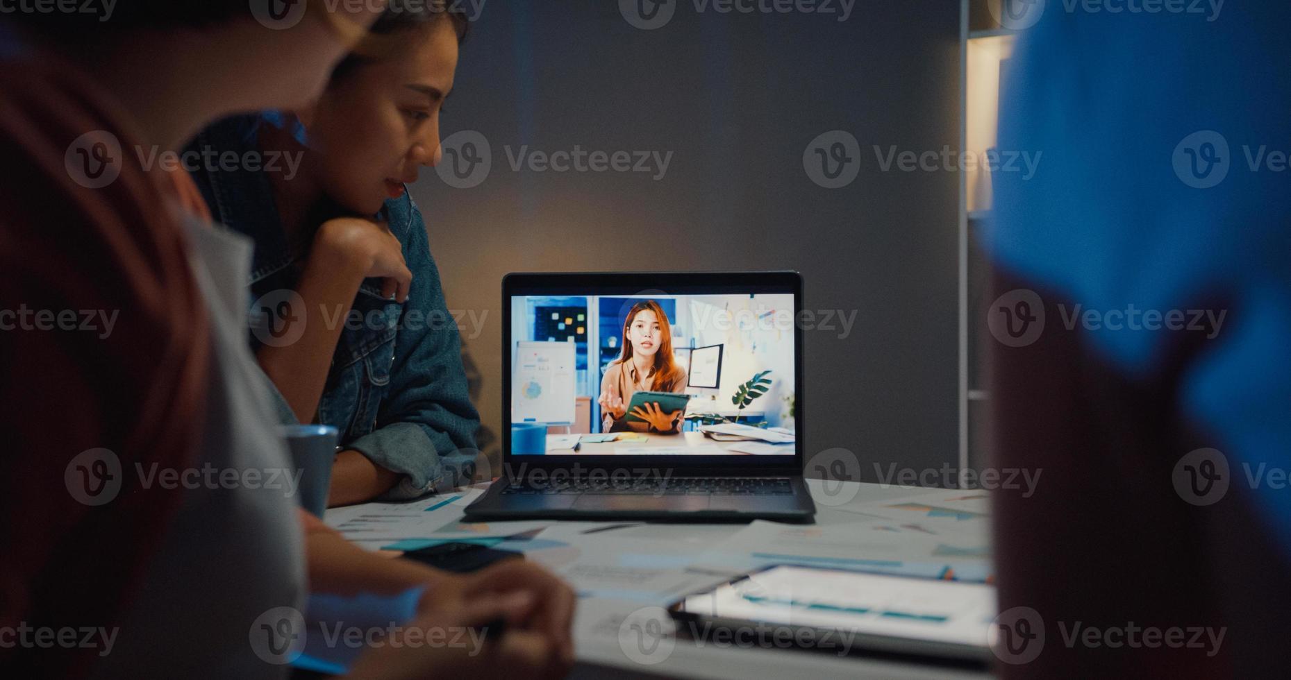 Asia businesswomen using laptop talk to colleagues about plan in video call meeting at home office. Working from house overload at night, remotely work, social distancing, quarantine for coronavirus. photo