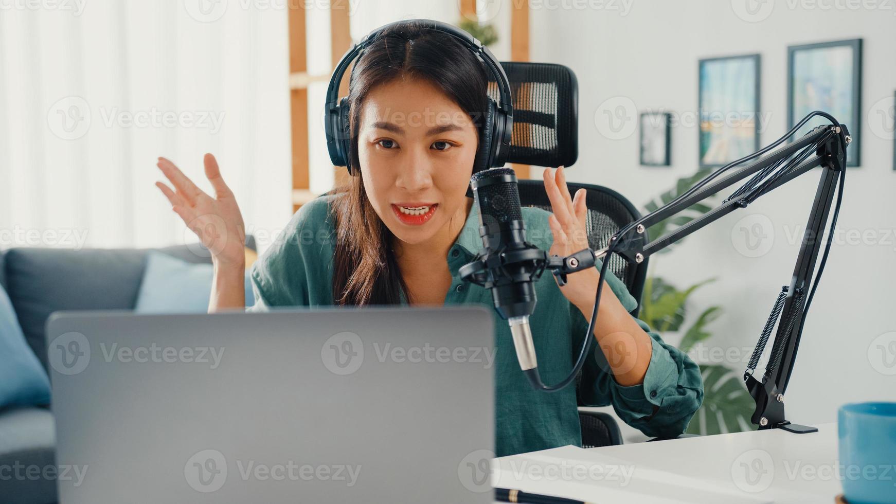 Happy asia girl record a podcast on her laptop computer with headphones and microphone talk with audience at her room. Female podcaster make audio podcast from her home studio, Stay at house concept. photo