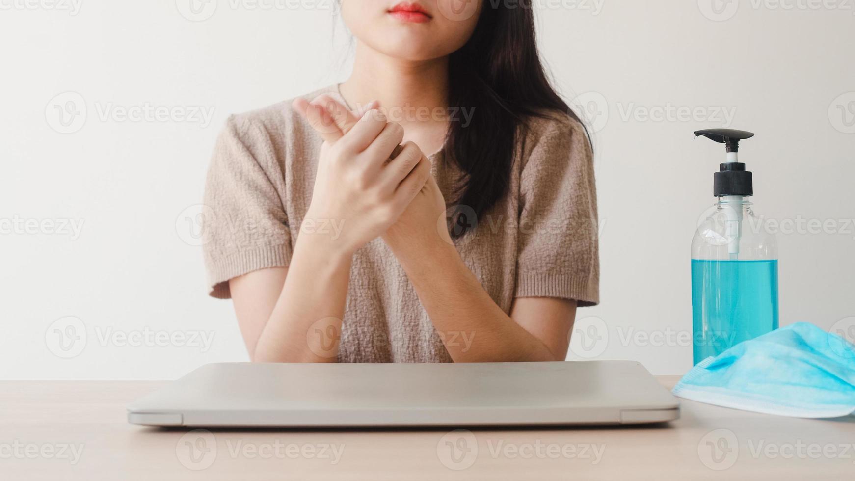 Mujer asiática que usa gel de alcohol desinfectante para manos lavarse las manos antes de abrir la computadora portátil para proteger el coronavirus. las mujeres empujan el alcohol para limpiar por higiene cuando el distanciamiento social se queda en casa y el tiempo de auto cuarentena foto