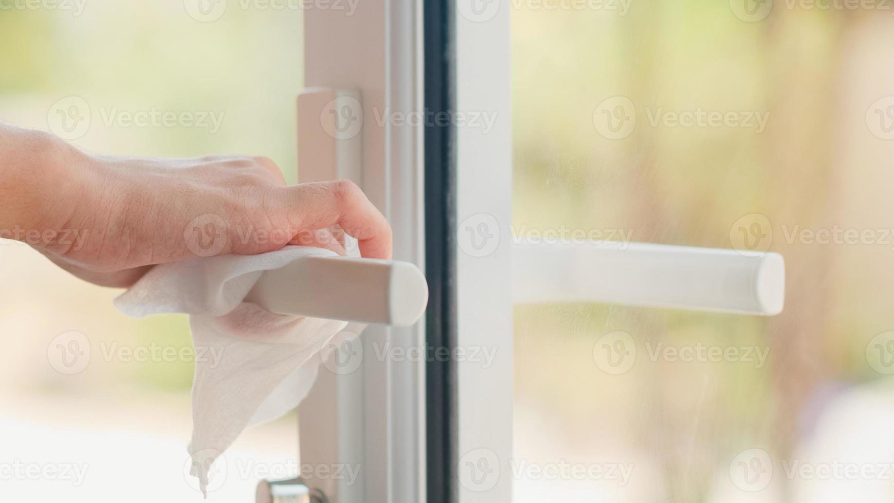 Mujer asiática usando spray de alcohol en el pomo de la puerta limpio de tejido antes de abrir la puerta para proteger el coronavirus. Hembra superficie limpia para higiene cuando el distanciamiento social permanece en casa y el tiempo de auto cuarentena. foto