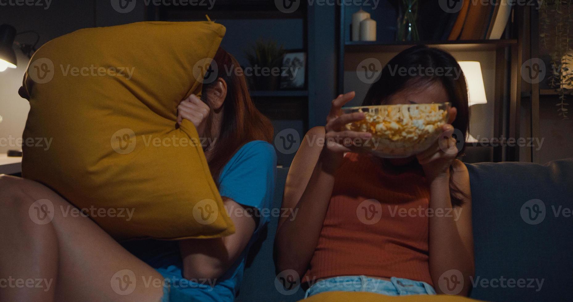 Attractive Asia couple ladies feel shock and fear moment eat popcorn watch horror online movie entertainment on sofa  in living room at home dark night. Weekend lifestyle activity quarantine concept. photo