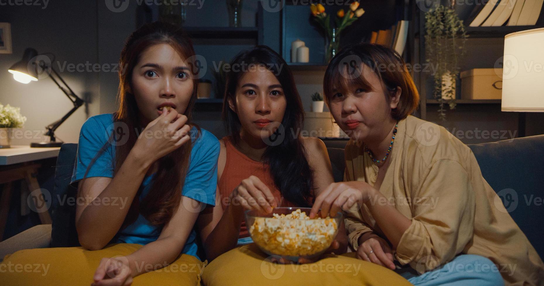 Group of attractive Asia lady girl freaking out fear and terrified moment eat popcorn watch horror online movie on couch in living room at home in night. Weekend lifestyle activity quarantine concept. photo