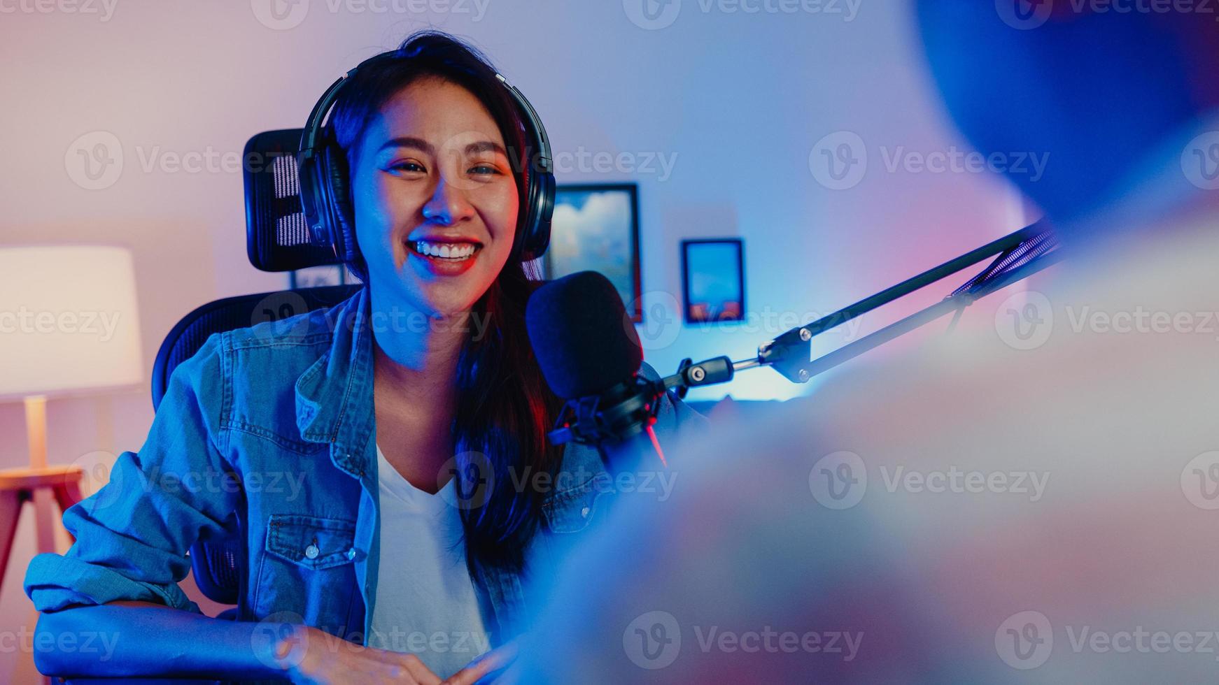 Happy asia girl host record podcast use microphone wear headphone with laptop interview guest conversation for content in her home studio at night. Sound equipment concept. Content creator concept. photo