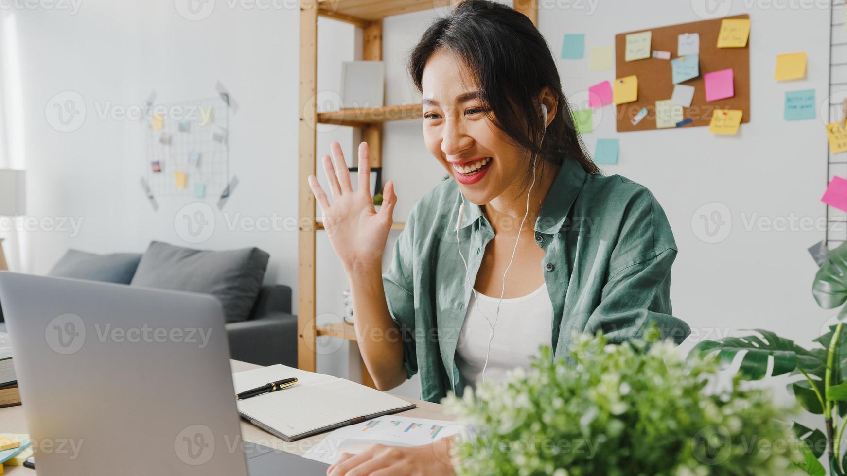 Asia businesswoman using laptop talk to colleagues about plan in video call while smart working from home at living room. Self-isolation, social distancing, quarantine for corona virus prevention. photo