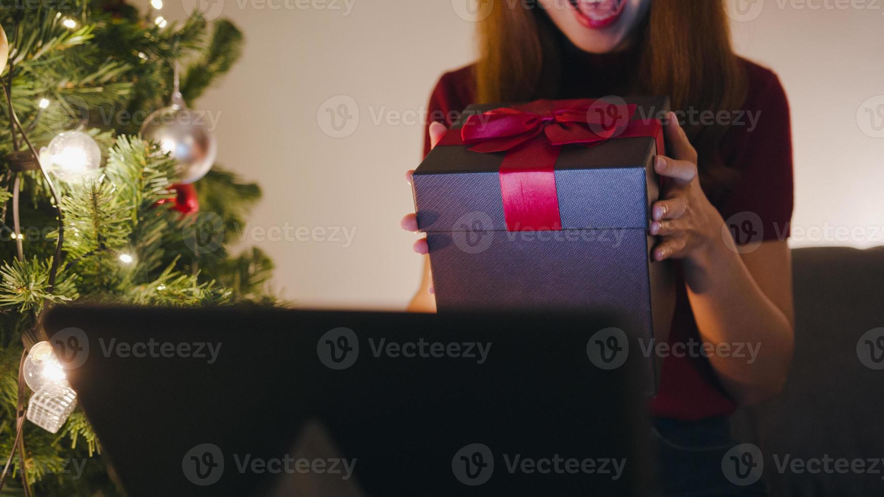 Young Asia female using tablet video call talking with couple with X'Mas present box, Christmas tree decorated with ornament in living room at home. Christmas night and New Year holiday festival. photo