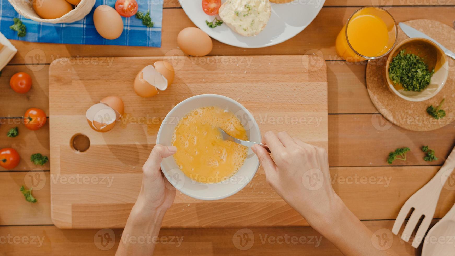 Hands of young Asian woman chef whisking egg into ceramic bowl cook omelette with vegetables on wooden board on kitchen table in house. Lifestyle healthy eat and traditional bakery. Top view shot. photo