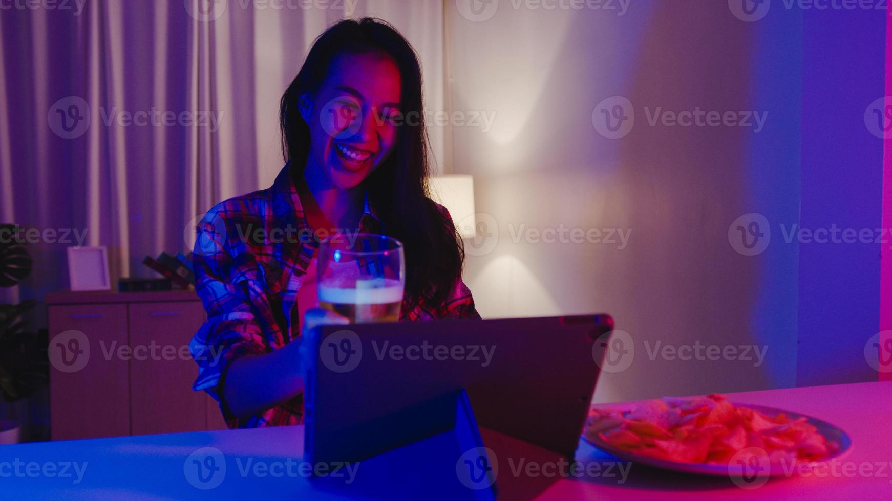 joven asiática bebiendo cerveza divirtiéndose momento feliz discoteca neón noche fiesta evento celebración en línea a través de videollamada en la sala de estar de casa. distanciamiento social, cuarentena para la prevención del coronavirus. foto