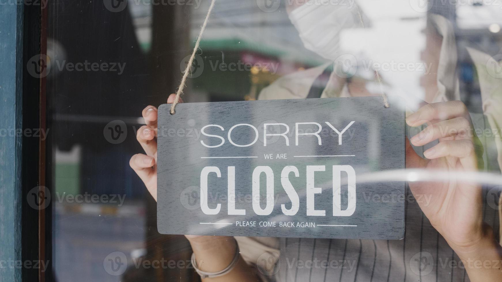 Young Asia girl wear face mask turning a sign from open to closed sign on glass door cafe after coronavirus lockdown quarantine. Owner small business, food and drink, business financial crisis concept photo