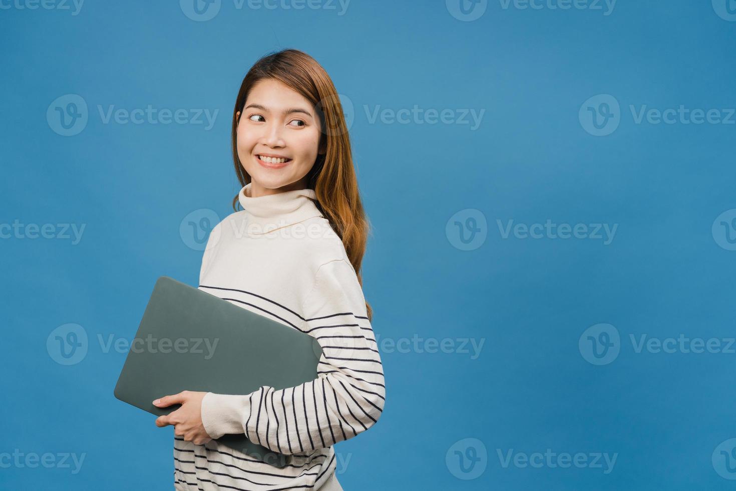 Young Asia lady hold laptop with positive expression, smiles broadly, dressed in casual clothing feeling happiness and stand isolated on blue background. Happy adorable glad woman rejoices success. photo