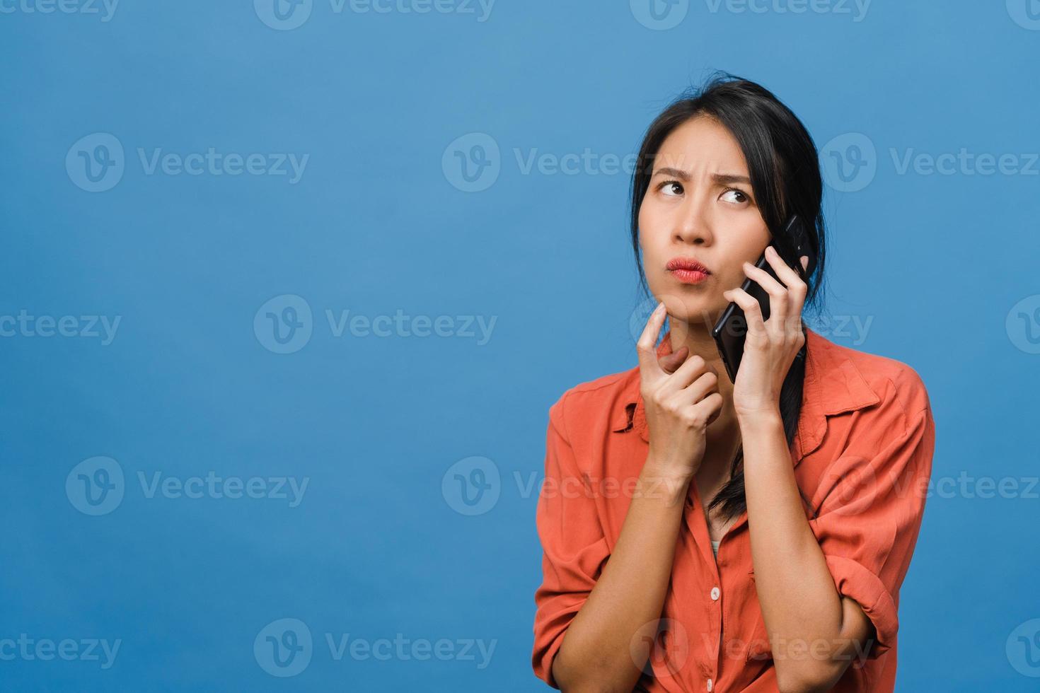 Jovencita asiática habla por teléfono con expresión negativa, gritos emocionados, gritos emocionales enojados en ropa casual y se para aislado sobre fondo azul con espacio de copia en blanco. concepto de expresión facial. foto