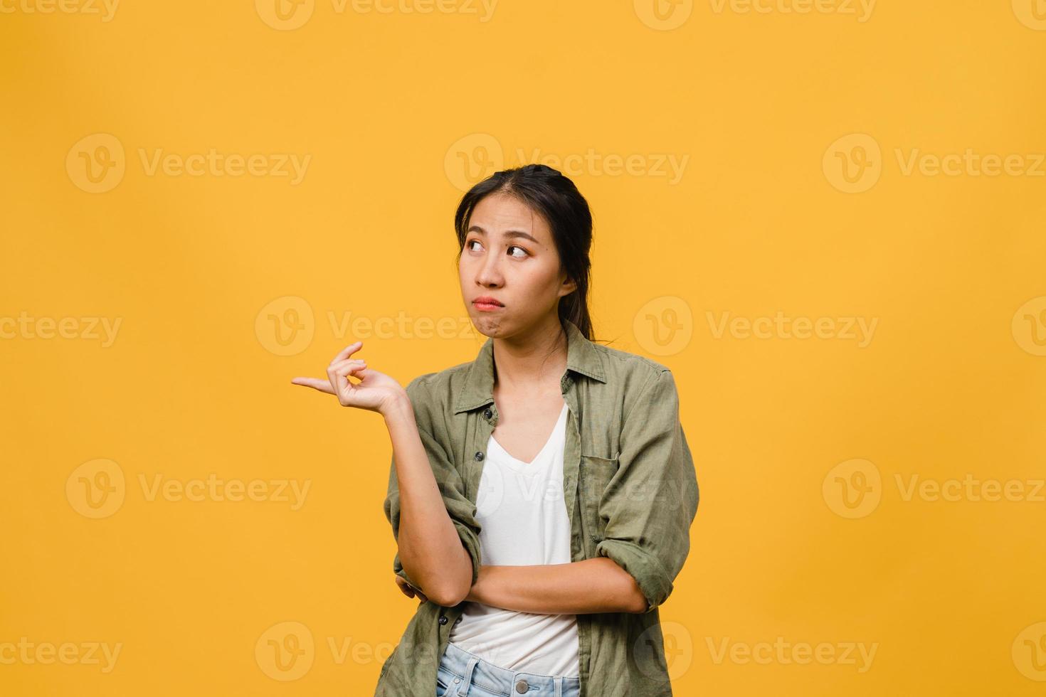 Joven mujer asiática muestra algo sorprendente en el espacio en blanco con expresión negativa, gritos emocionados, llorando enojado emocional en ropa casual aislada sobre fondo amarillo. concepto de expresión facial. foto