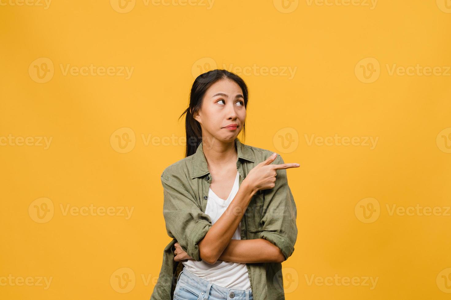 Joven mujer asiática muestra algo sorprendente en el espacio en blanco con expresión negativa, gritos emocionados, llorando enojado emocional en ropa casual aislada sobre fondo amarillo. concepto de expresión facial. foto