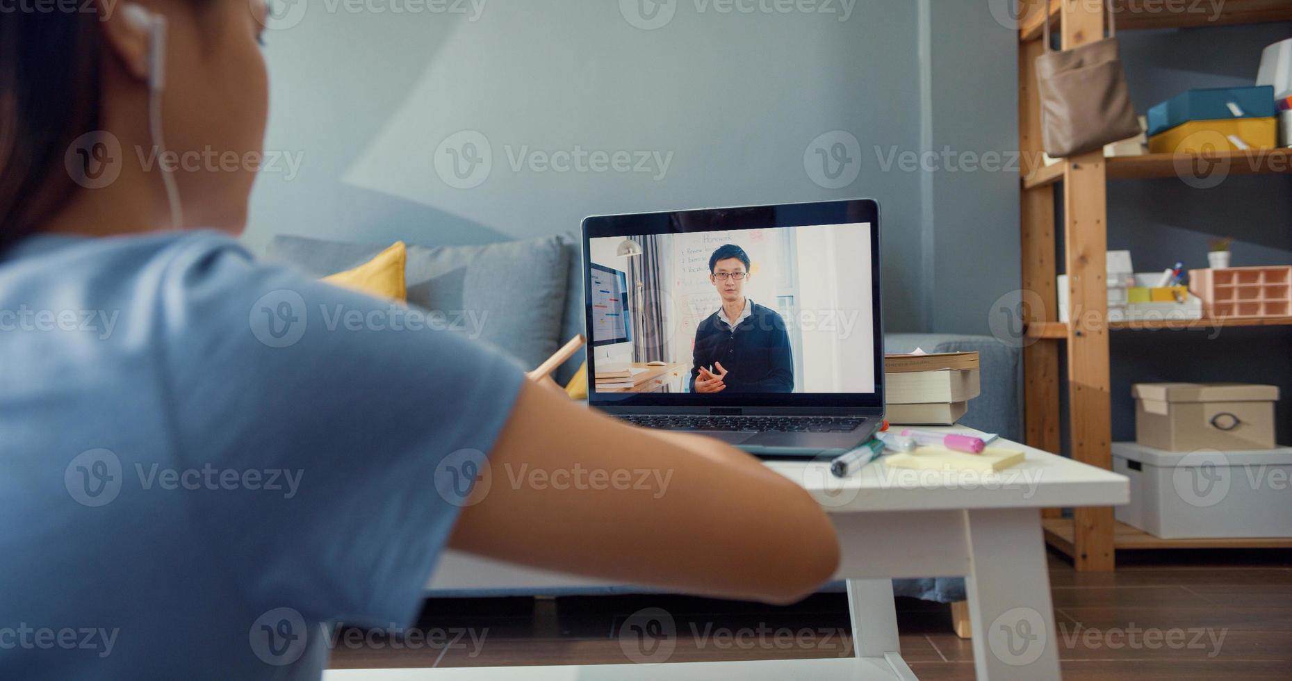 Close-up joven asiática con auriculares de uso casual usar videollamada de computadora portátil aprender en línea con un tutor en la sala de estar de la casa. Aislar el concepto de pandemia de coronavirus de educación en línea e-learning. foto