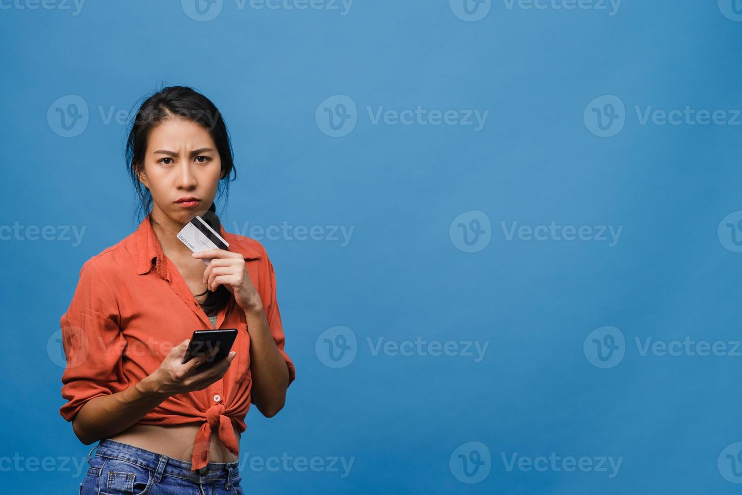 Young Asia lady using phone and credit bank card with negative expression, excited screaming, cry emotional angry in casual cloth and stand isolated on blue background. Facial expression concept. photo