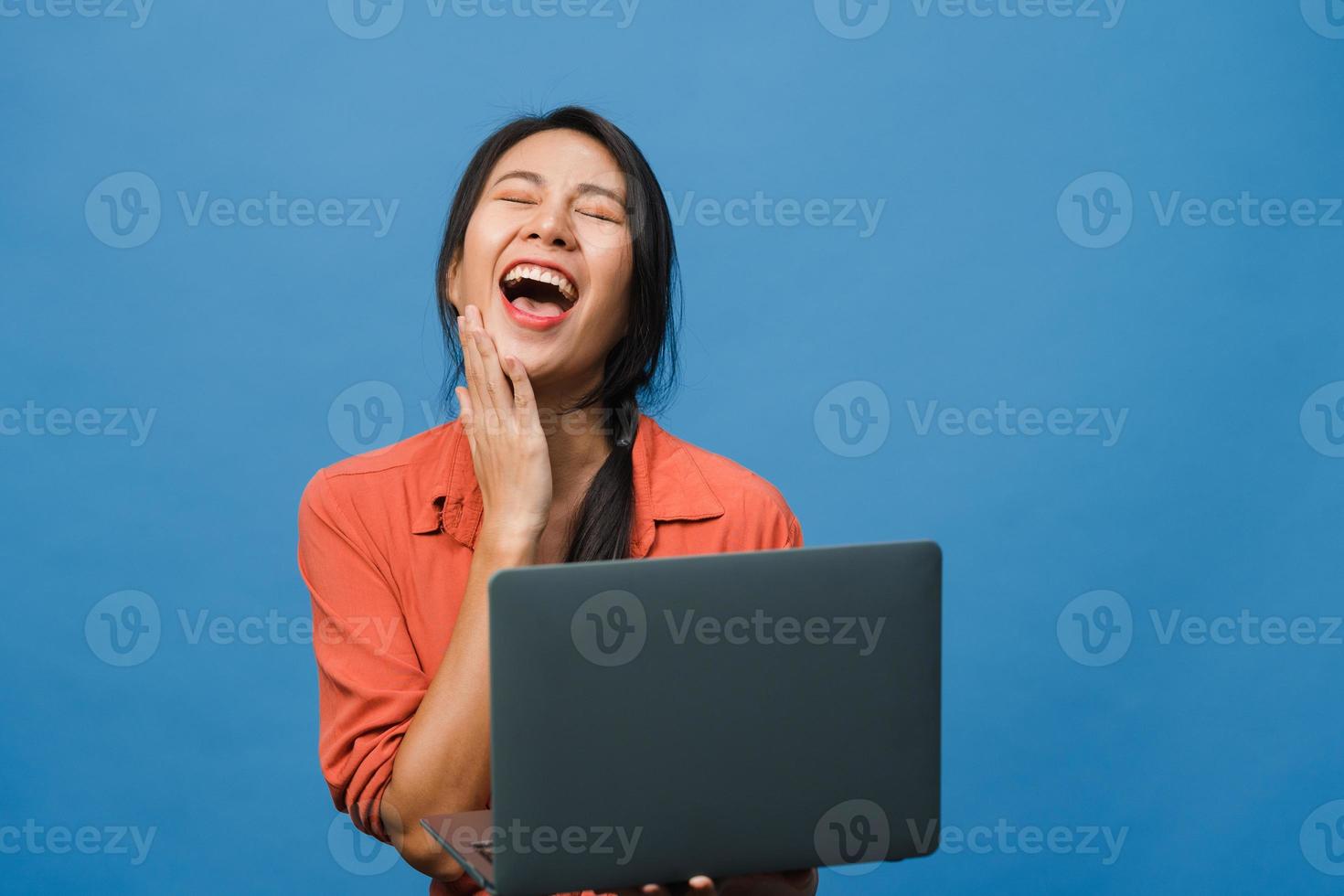 Jovencita asiática usando laptop con expresión positiva, sonríe ampliamente, vestida con ropa casual sintiendo felicidad y parada aislada sobre fondo azul. feliz adorable mujer alegre se regocija con el éxito. foto