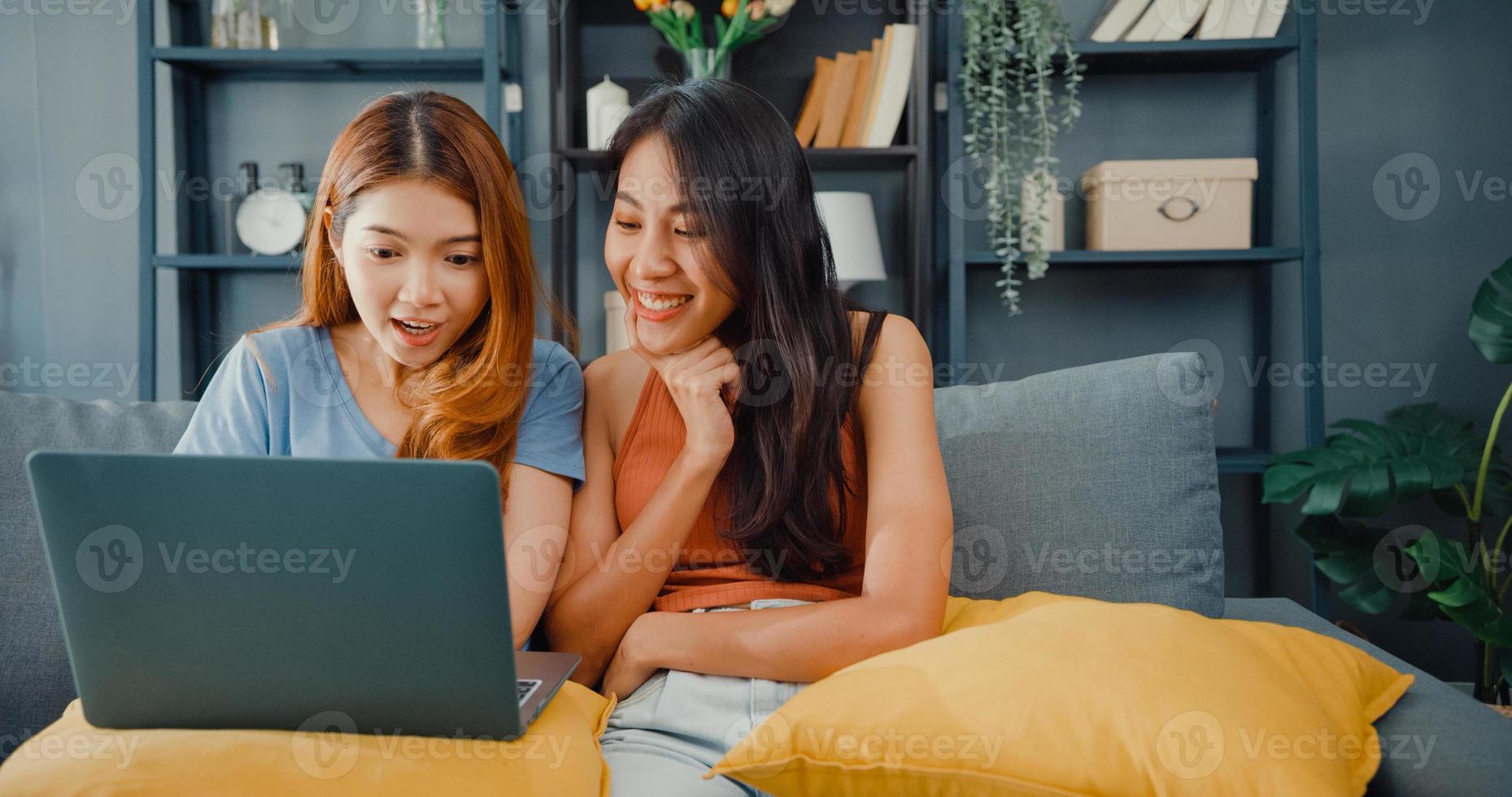 Two Asia lesbian women site on couch together looking at laptop screen in living room at home together. Happy couple roommate ladies enjoy web surfing online shopping, Lifestyle woman at home concept. photo