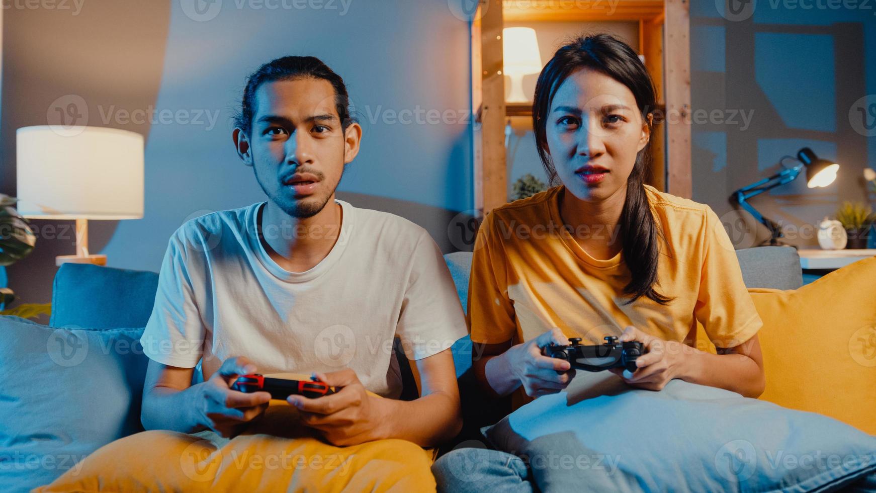 Happy asia young couple man and woman sit couch use joystick controller play video game spend fun time together in living room at night. Asian married couple family lifestyle, Stay at home concept. photo