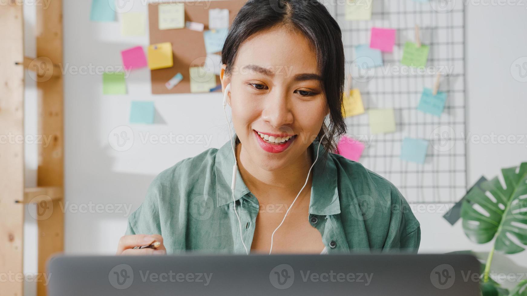 Asia businesswoman using laptop talk to colleagues about plan in video call while smart working from home at living room. Self-isolation, social distancing, quarantine for corona virus prevention. photo