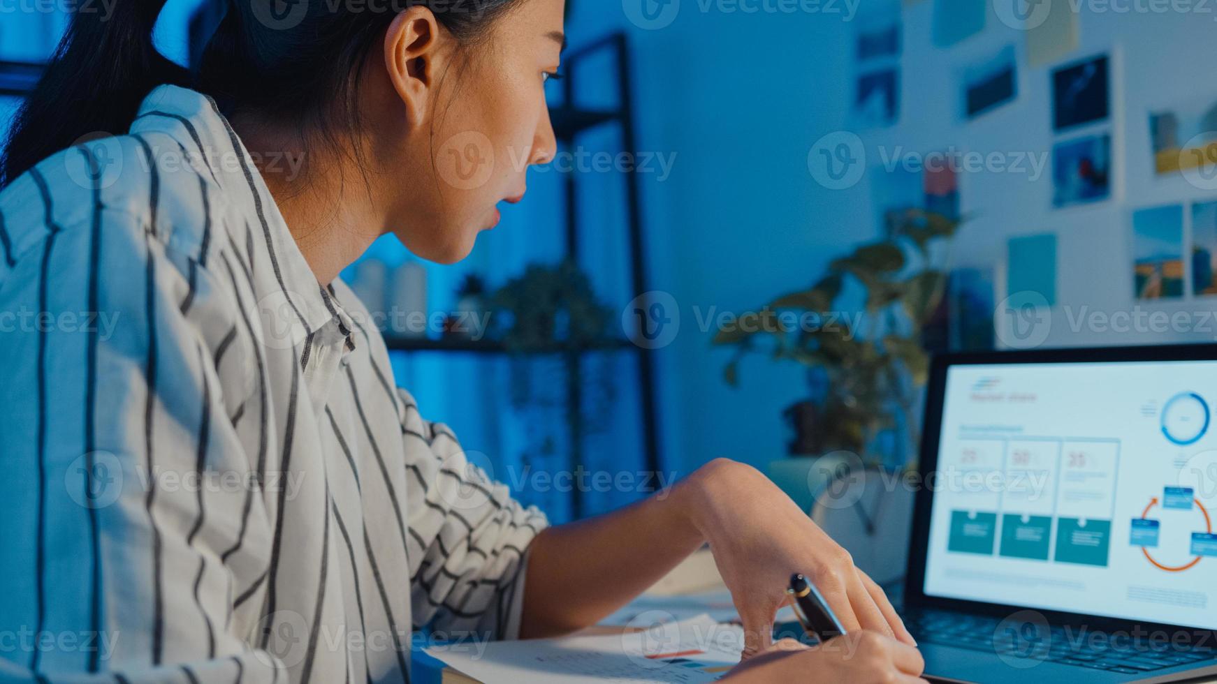 joven mujer de negocios de asia freelance centrarse en la computadora portátil escribir hoja de cálculo finanzas gráfico gráfico de cuenta plan de mercado en computadora portátil y tableta en la noche de la casa. chica estudiante aprende en línea, trabaja desde el concepto de hogar. foto