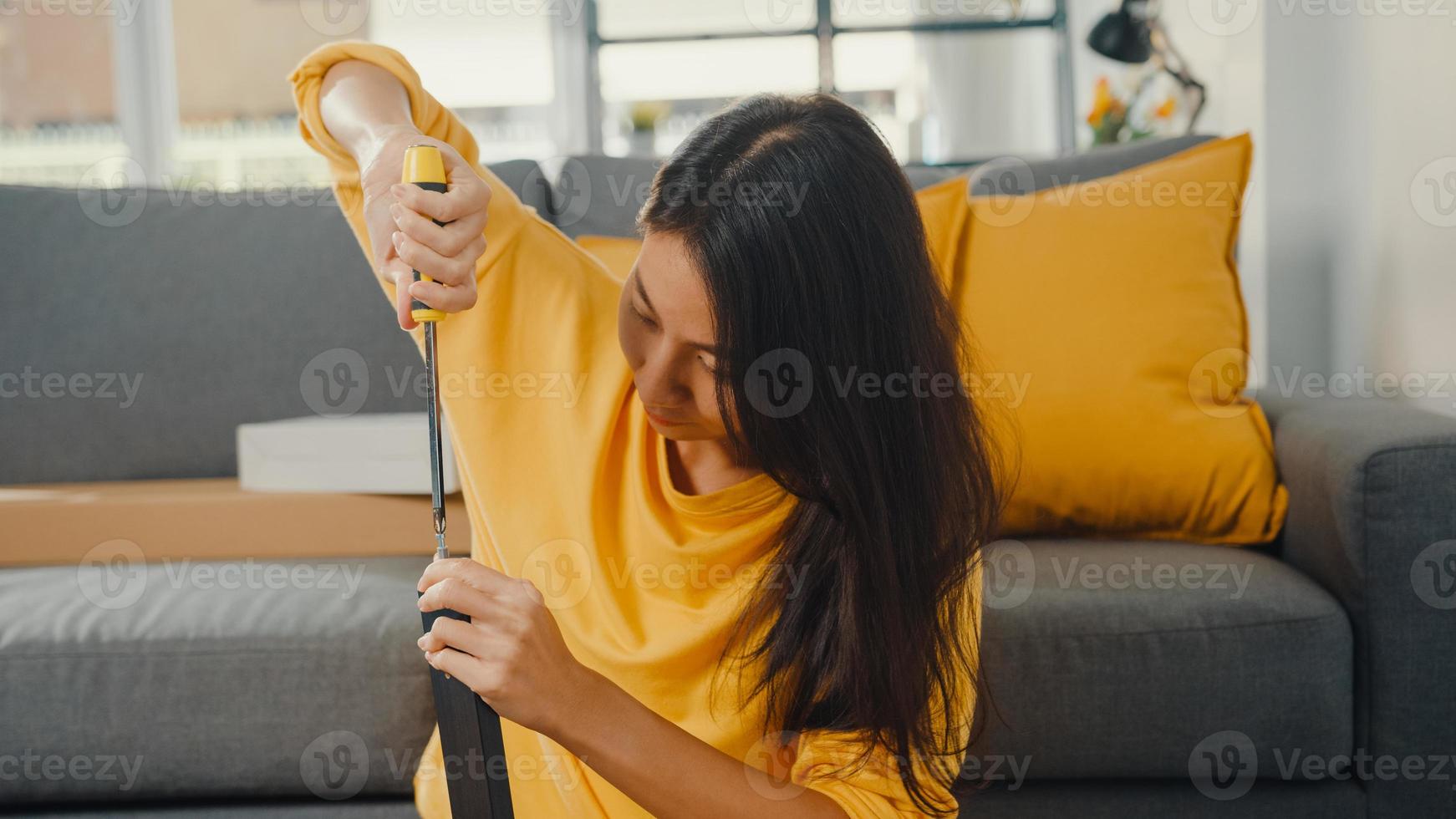 Feliz joven asiática desempacando la caja y leyendo las instrucciones para ensamblar muebles nuevos decorar la mesa de construcción de la casa con caja de cartón en la sala de estar de casa. foto