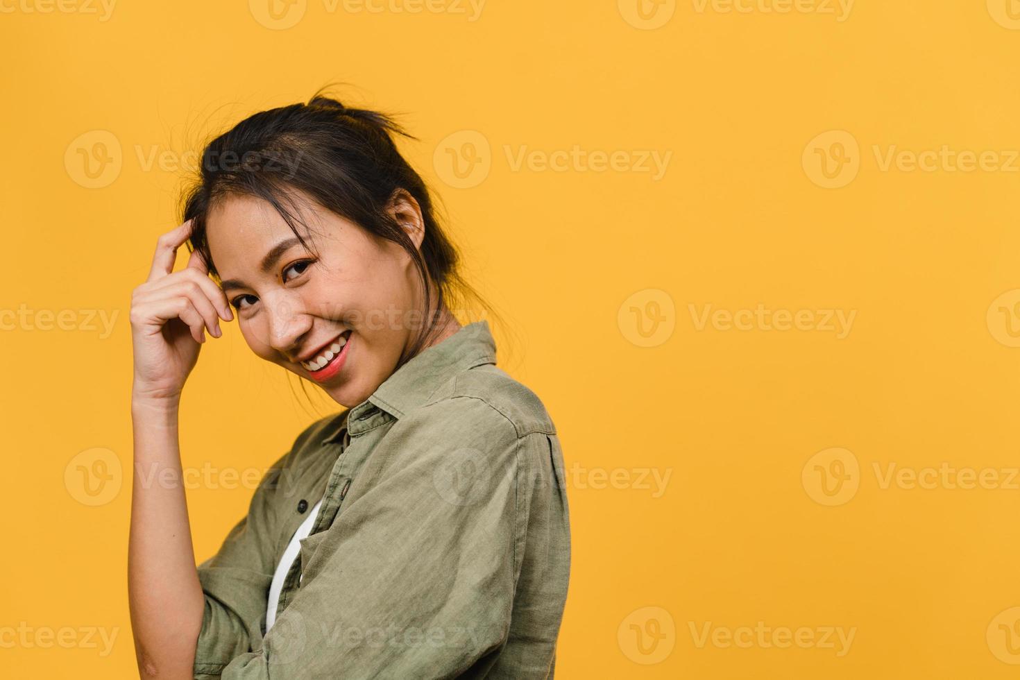 Jovencita asiática con expresión positiva, sonrisa amplia, vestida con ropa casual y mirando a cámara sobre fondo amarillo. feliz adorable mujer alegre se regocija con el éxito. concepto de expresión facial. foto