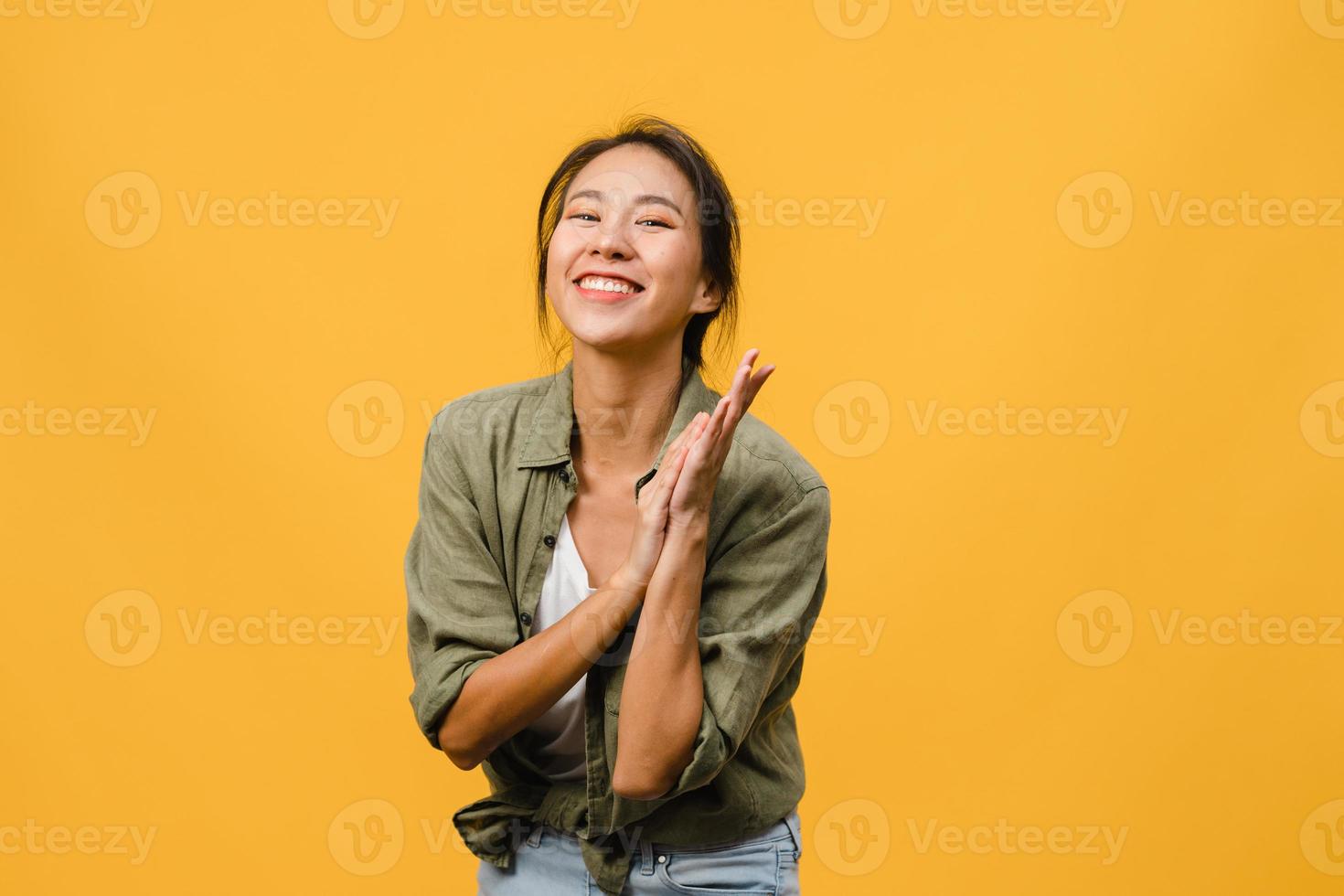 Jovencita asiática con expresión positiva, sonrisa amplia, vestida con ropa casual y mirando a cámara sobre fondo amarillo. feliz adorable mujer alegre se regocija con el éxito. concepto de expresión facial. foto