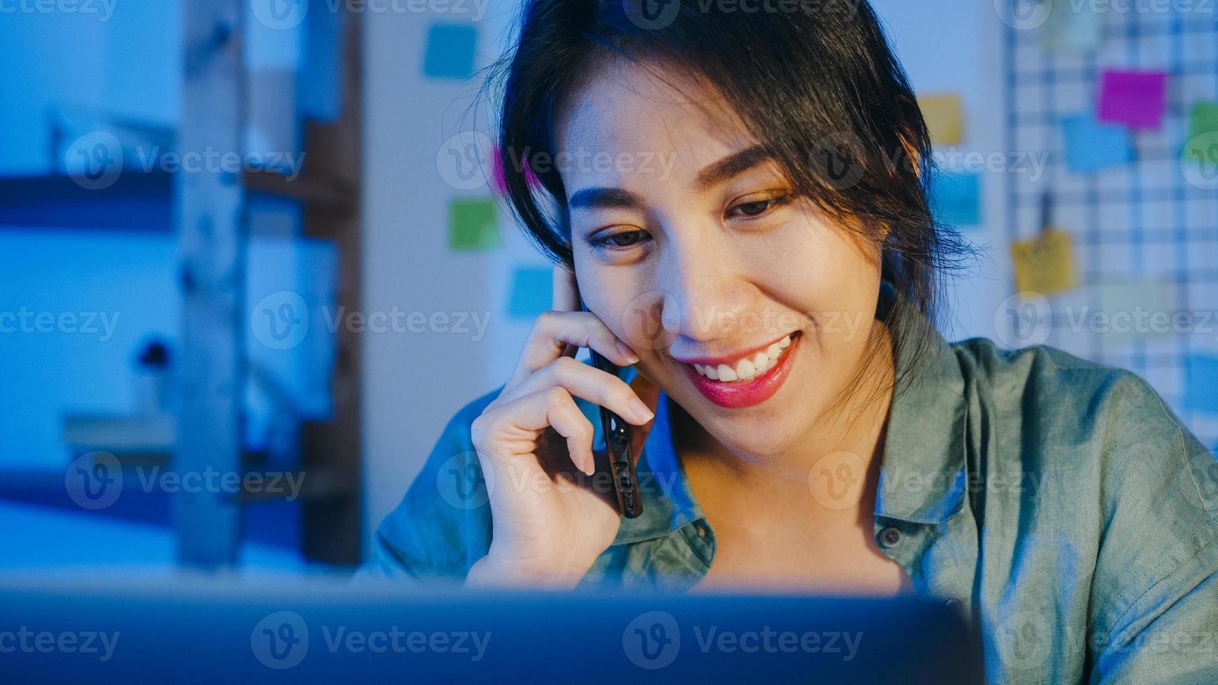 Freelance Asia women using laptop talk on phone busy entrepreneur working distantly in living room. Working from house overload at night, remotely work, social distancing, quarantine for coronavirus. photo