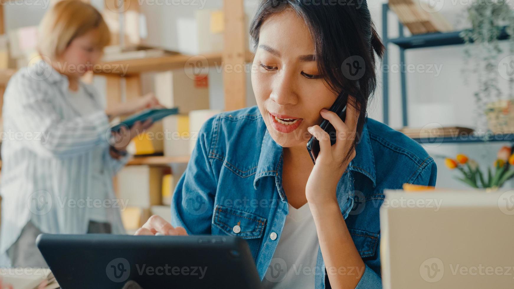 Young Asia businesswomen using mobile phone call receiving purchase order and check product on stock work at home office. Small business owner, online market delivery, lifestyle freelance concept. photo