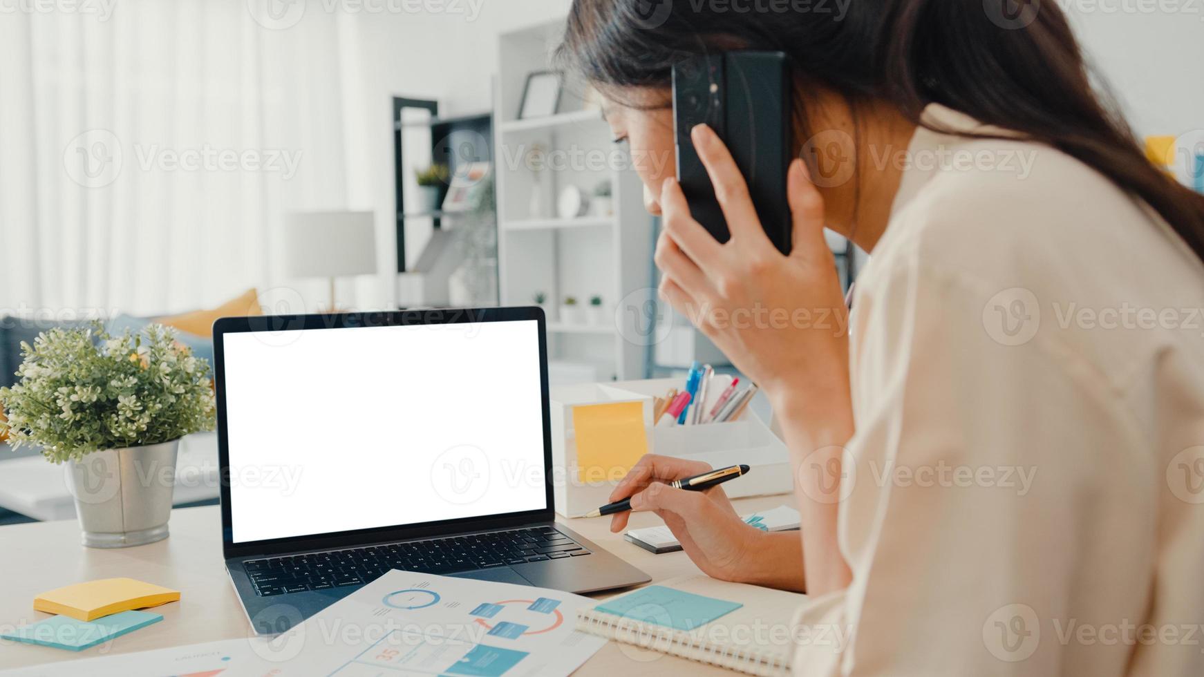 Joven empresaria asiática usa un teléfono inteligente con una pantalla en blanco en blanco simulado para mostrar texto publicitario mientras trabaja de manera inteligente desde casa en la sala de estar. tecnología chroma key, concepto de diseño de marketing. foto