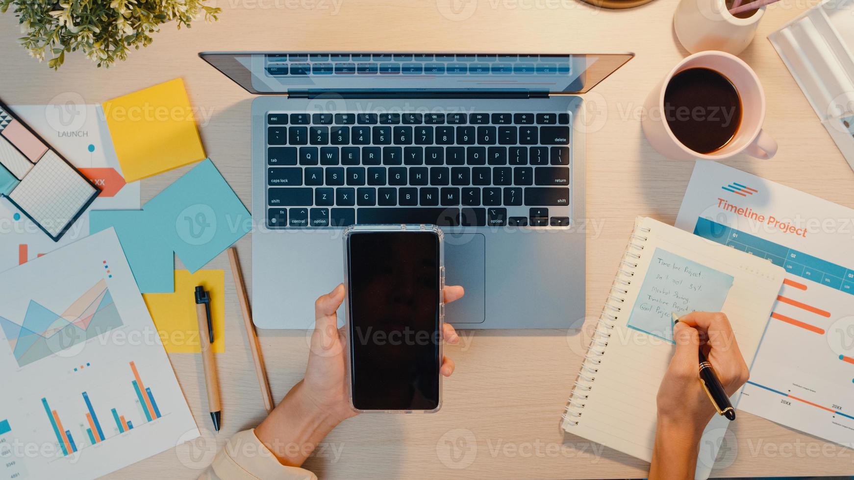 Vista superior del teléfono de uso independiente de la joven asiática con pantalla negra en blanco, pantalla simulada para texto publicitario y enfoque en la computadora portátil, escriba la hoja de trabajo, gráfico de finanzas, gráfico de cuenta, plan de mercado, en la noche de la oficina foto