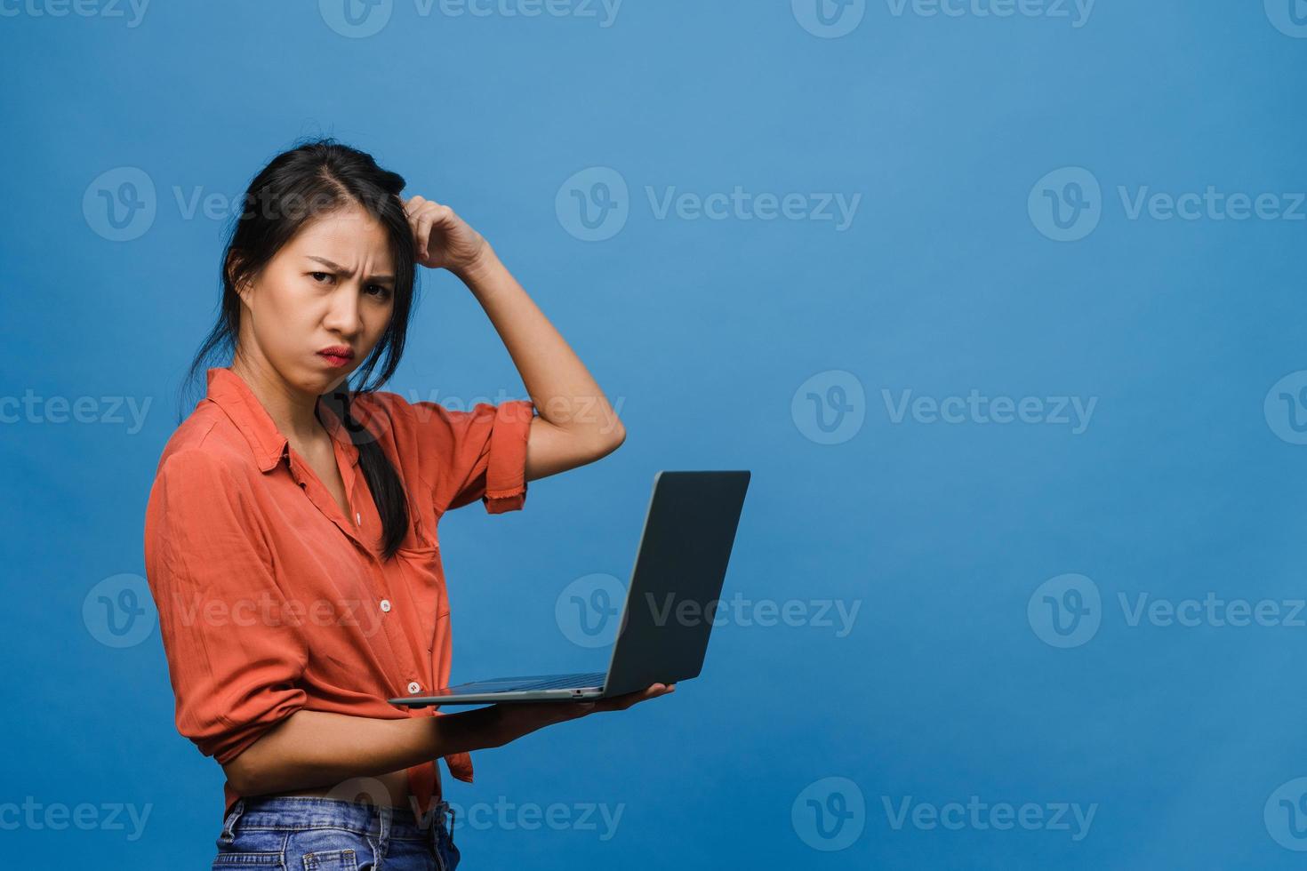 Young Asia lady using laptop with negative expression, excited screaming, cry emotional angry in casual cloth and stand isolated on blue background with blank copy space. Facial expression concept. photo